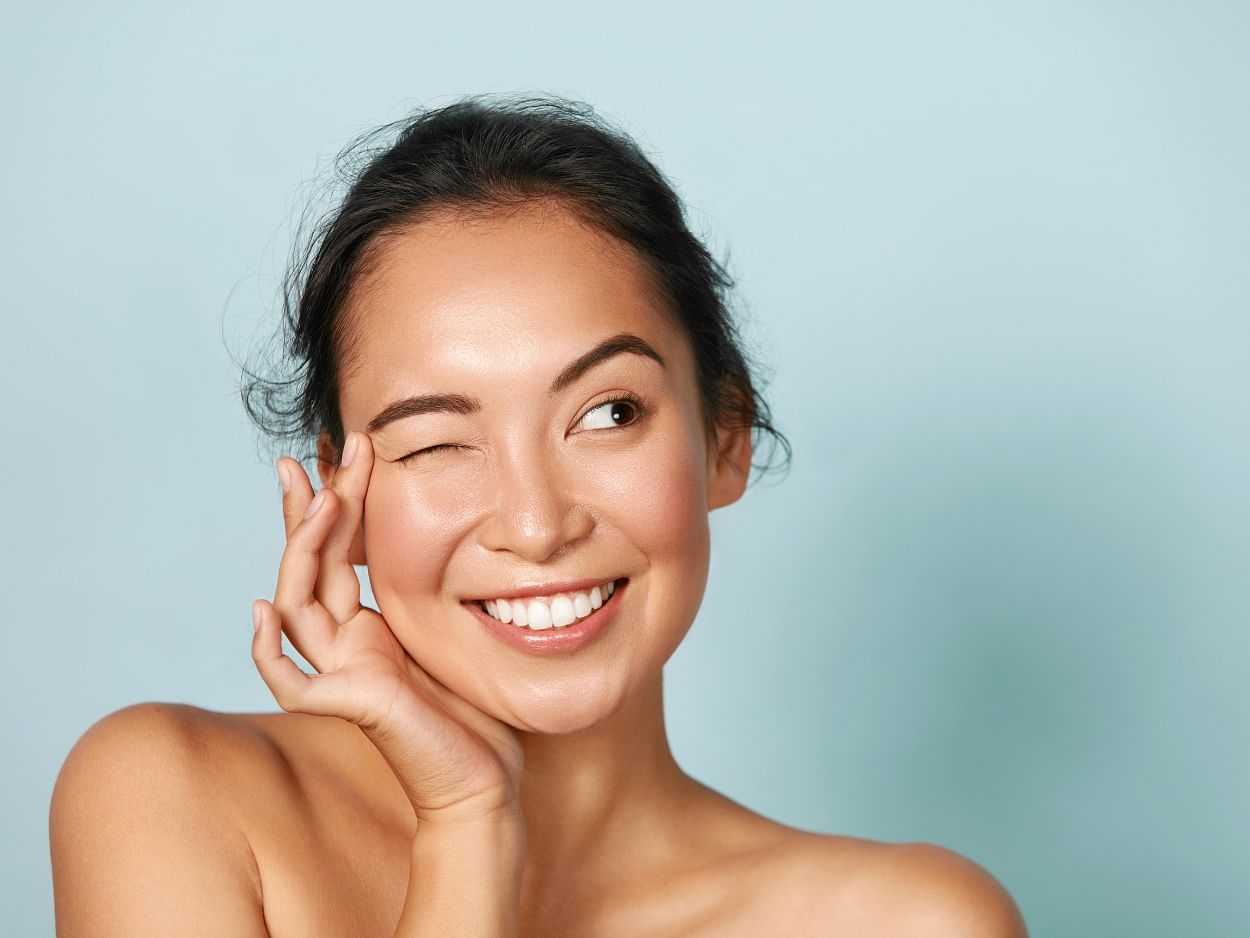 Woman smiling with hand on face against a blue background.
