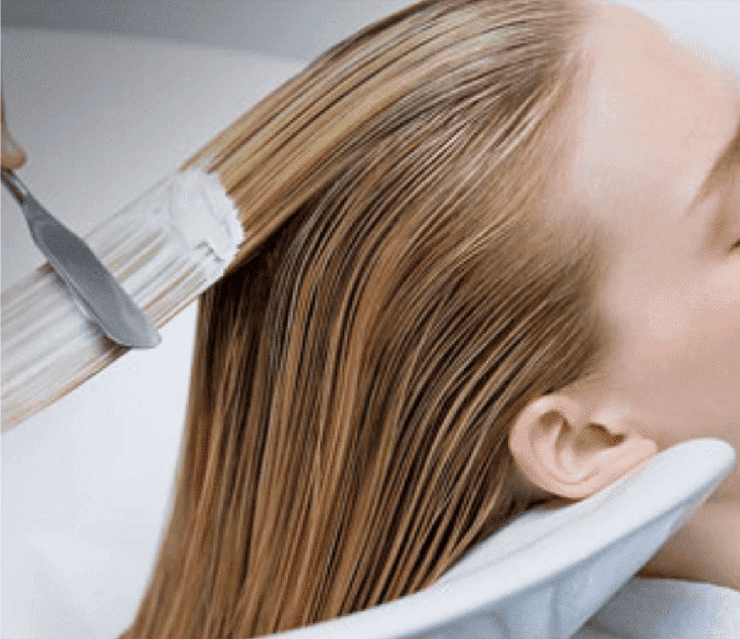 Applying hair color treatment to long blonde hair at a salon.